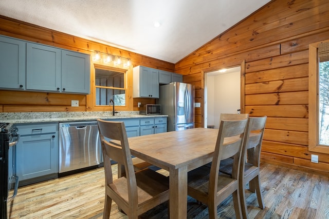 kitchen with black appliances, light wood-type flooring, light stone countertops, wooden walls, and vaulted ceiling