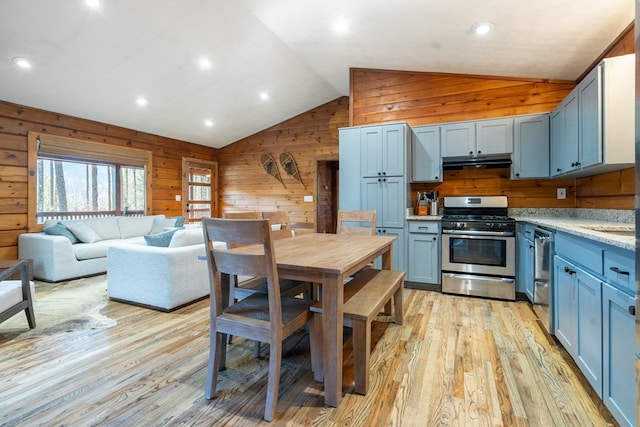 kitchen featuring stainless steel appliances, wooden walls, blue cabinets, lofted ceiling, and light hardwood / wood-style flooring