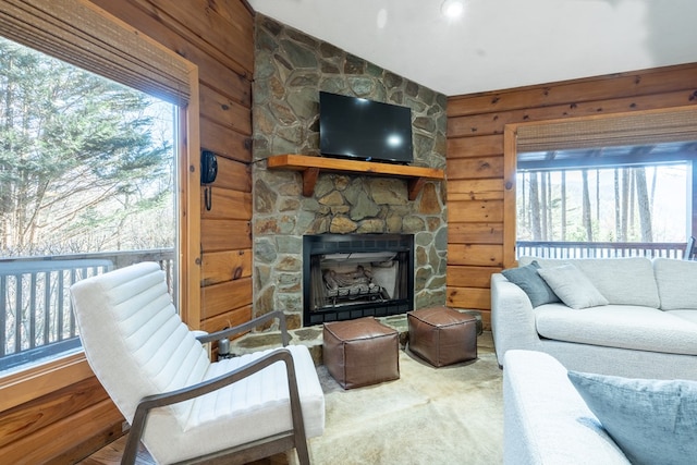 living room with a stone fireplace, plenty of natural light, wooden walls, and vaulted ceiling