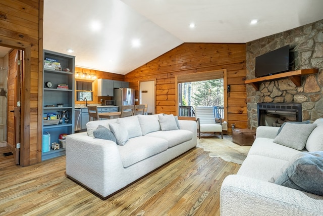 living room featuring a stone fireplace, wood walls, lofted ceiling, and light hardwood / wood-style floors