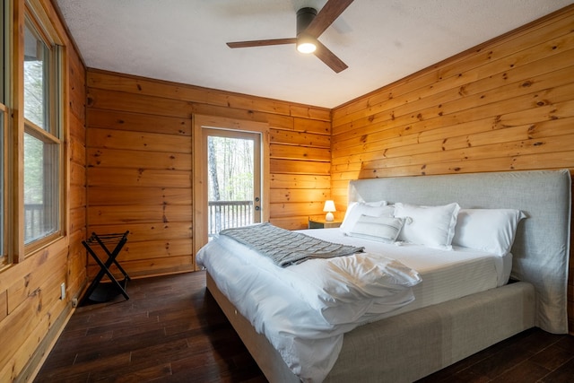 bedroom with ceiling fan, access to exterior, wood walls, and dark hardwood / wood-style flooring