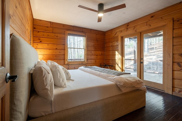 bedroom with dark hardwood / wood-style flooring, wood walls, multiple windows, and access to exterior