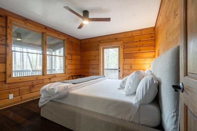 bedroom with access to outside, dark hardwood / wood-style flooring, wood walls, and ceiling fan