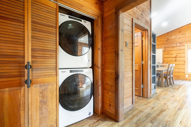 clothes washing area with light wood-type flooring, wooden walls, and stacked washer and dryer