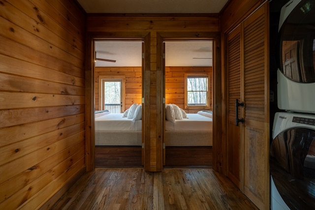 corridor with stacked washing maching and dryer, dark wood-type flooring, and wood walls