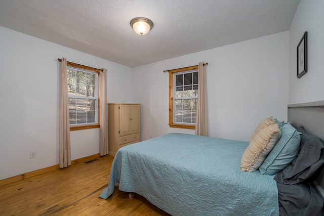 bedroom with multiple windows, wood-type flooring, and a textured ceiling