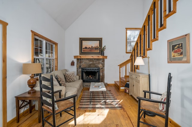 living room featuring a stone fireplace, high vaulted ceiling, and light wood-type flooring