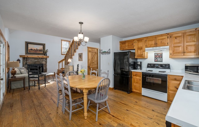 kitchen with a stone fireplace, hanging light fixtures, electric range, black fridge, and light wood-type flooring