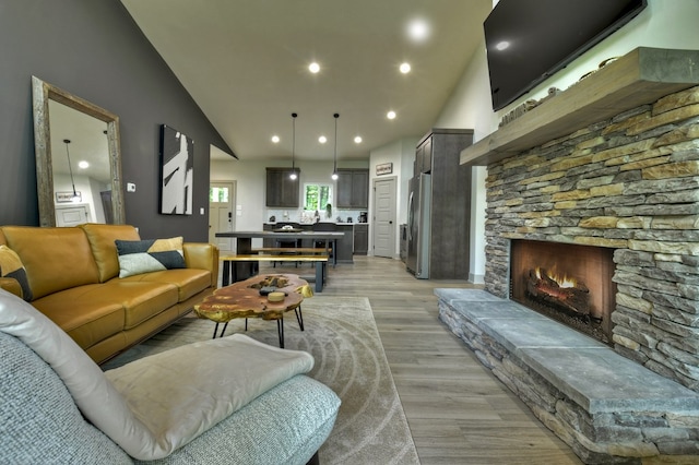 living room featuring recessed lighting, a stone fireplace, light wood-style flooring, and high vaulted ceiling