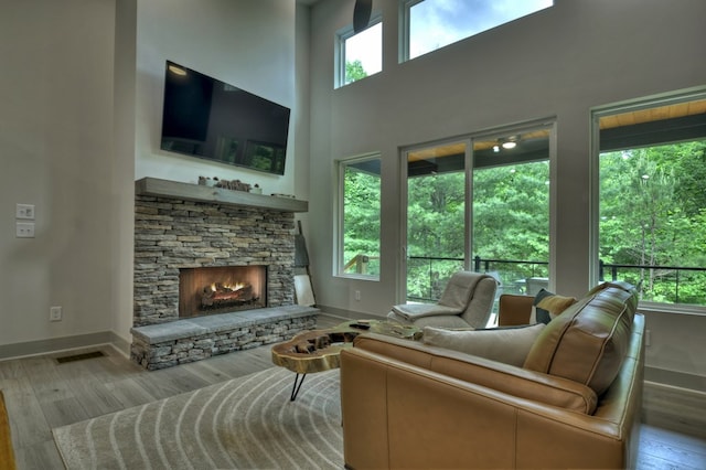 living area with visible vents, baseboards, a fireplace, a high ceiling, and wood finished floors