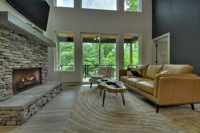 living area featuring a stone fireplace, wood finished floors, a high ceiling, and a healthy amount of sunlight