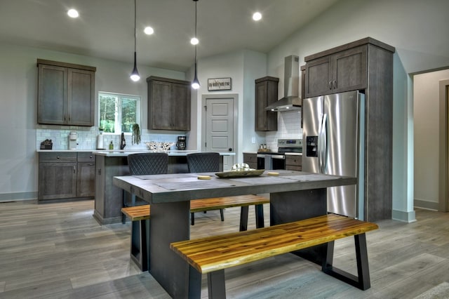 kitchen featuring wall chimney range hood, dark brown cabinets, light wood finished floors, and stainless steel appliances