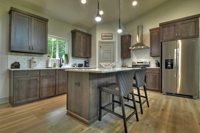 kitchen featuring light wood finished floors, wall chimney exhaust hood, appliances with stainless steel finishes, and a center island