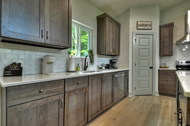 kitchen with light wood-style flooring, a sink, decorative backsplash, appliances with stainless steel finishes, and wall chimney range hood