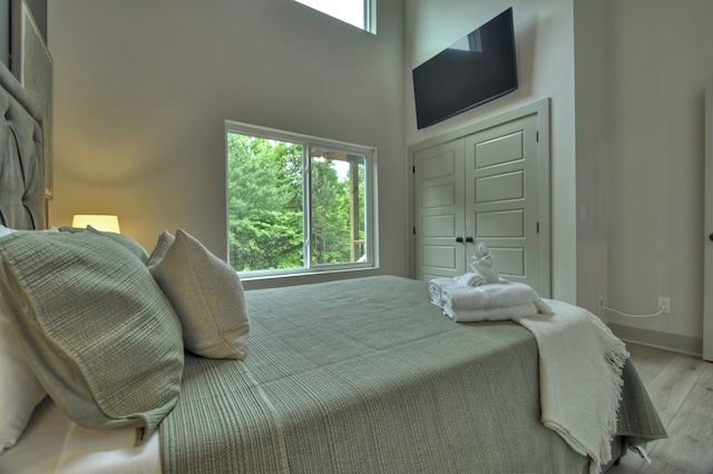 bedroom with baseboards, a high ceiling, and light wood-style flooring