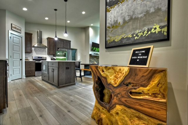 kitchen featuring wall chimney range hood, backsplash, fridge, light wood finished floors, and stainless steel electric range oven