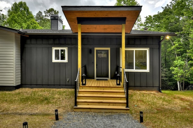 doorway to property featuring a porch, board and batten siding, and a chimney