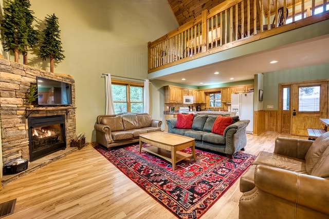 living room featuring a stone fireplace, wooden walls, a towering ceiling, and light hardwood / wood-style floors