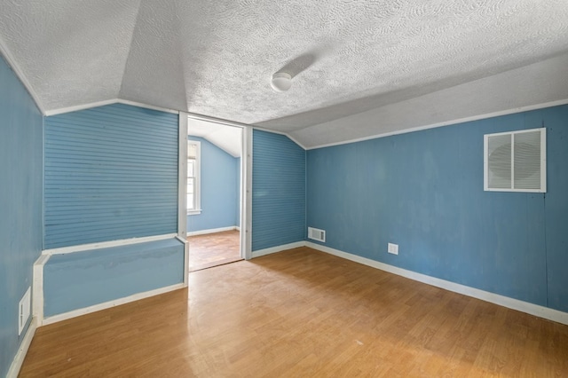 additional living space featuring wood-type flooring, a textured ceiling, and vaulted ceiling