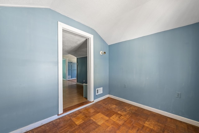 unfurnished room with dark parquet flooring, a textured ceiling, and lofted ceiling