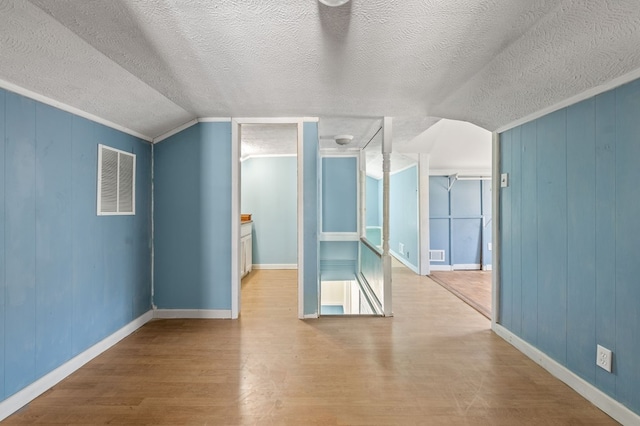 additional living space featuring wood-type flooring, a textured ceiling, vaulted ceiling, and wooden walls