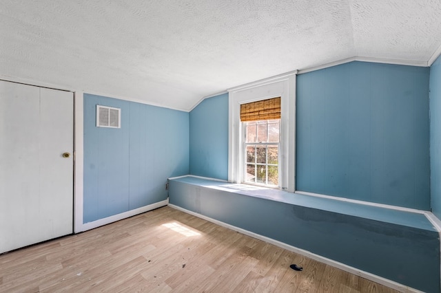 additional living space with light wood-type flooring, a textured ceiling, and vaulted ceiling