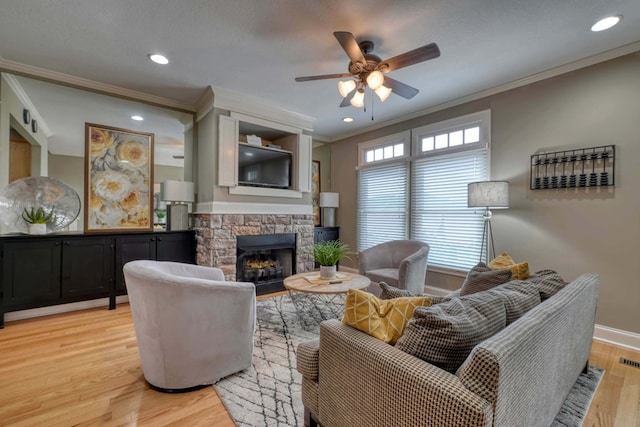 living room featuring crown molding, a fireplace, light wood-style floors, and ceiling fan