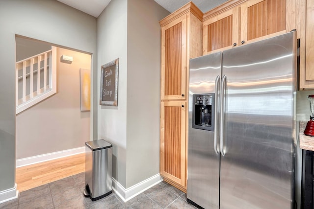 kitchen featuring tile patterned floors, stainless steel fridge with ice dispenser, light brown cabinets, and baseboards