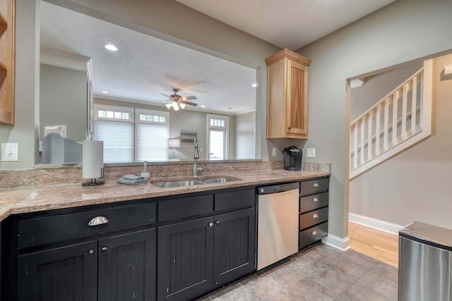 kitchen featuring a sink, light stone counters, stainless steel dishwasher, baseboards, and ceiling fan