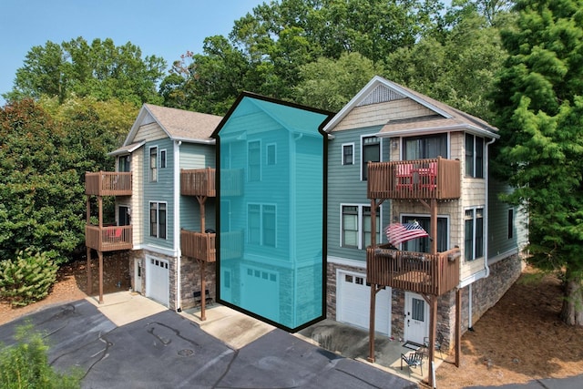 view of front of property with a garage, stone siding, a balcony, and driveway