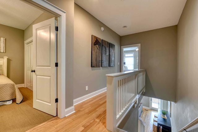 hallway with an upstairs landing, baseboards, and light wood finished floors