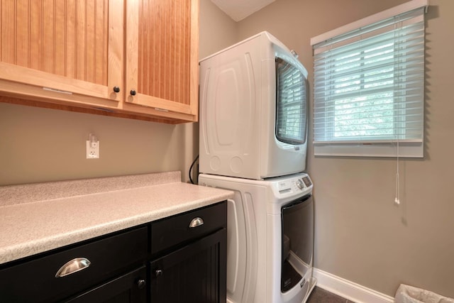 clothes washing area featuring cabinet space, stacked washer and clothes dryer, and baseboards