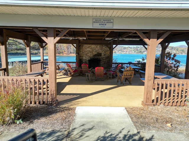 view of patio / terrace featuring a gazebo, a water view, an outdoor stone fireplace, and a ceiling fan