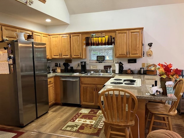 kitchen with lofted ceiling, kitchen peninsula, a breakfast bar, appliances with stainless steel finishes, and light hardwood / wood-style floors