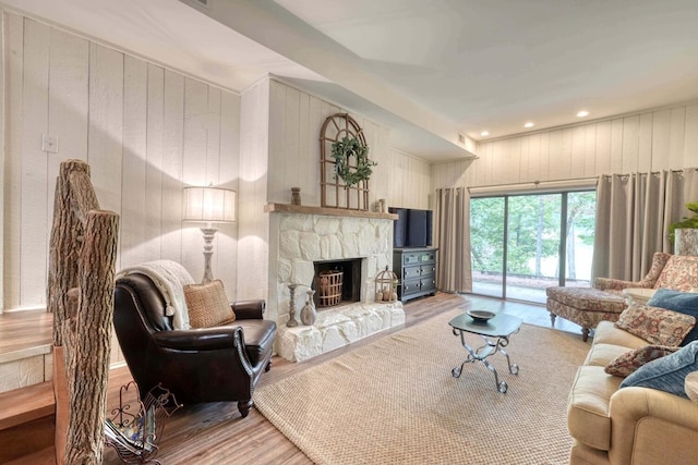 living room with wood-type flooring, a stone fireplace, and wooden walls