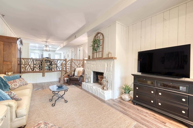 living room featuring a stone fireplace, light wood-type flooring, and wood walls