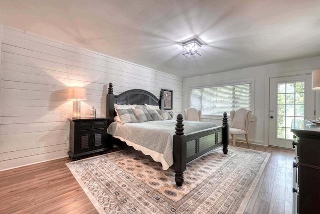 bedroom with access to outside, wooden walls, and hardwood / wood-style flooring