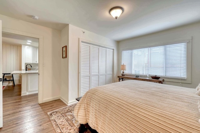 bedroom featuring a closet, baseboards, a sink, and light wood finished floors