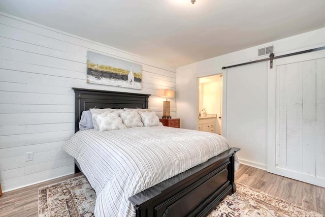 bedroom featuring a barn door, wooden walls, light wood-type flooring, and ensuite bath