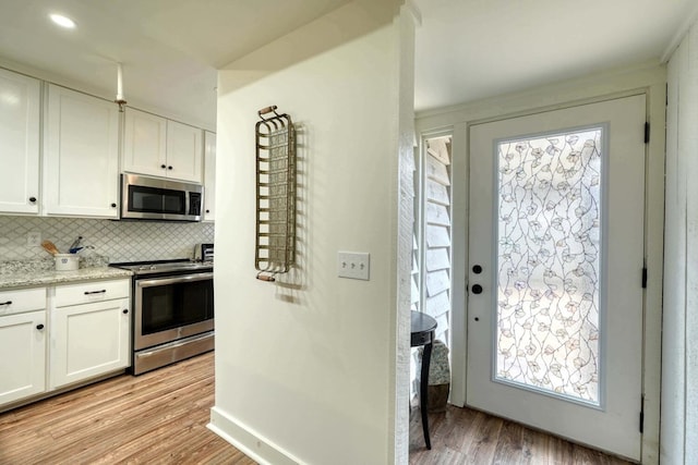 kitchen with light hardwood / wood-style floors, white cabinetry, decorative backsplash, appliances with stainless steel finishes, and light stone countertops