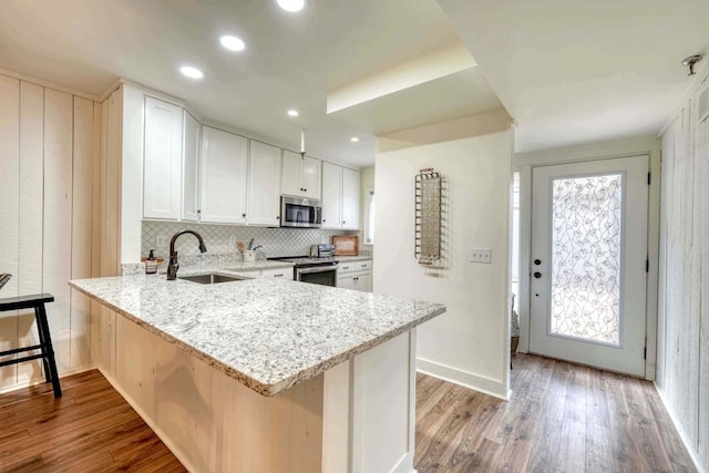 kitchen featuring a sink, light stone counters, white cabinets, appliances with stainless steel finishes, and wood finished floors