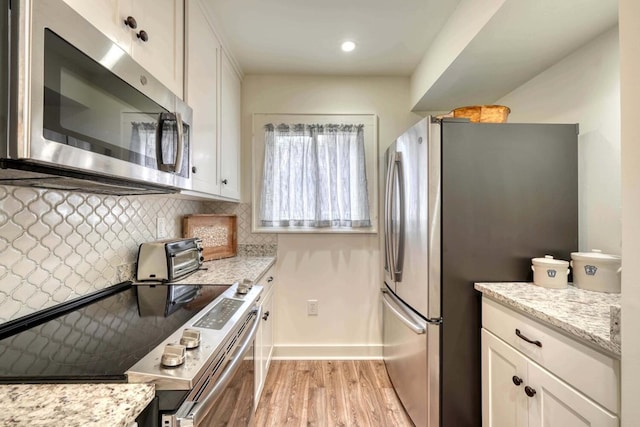 kitchen featuring stainless steel appliances, tasteful backsplash, white cabinetry, light wood-style floors, and light stone counters
