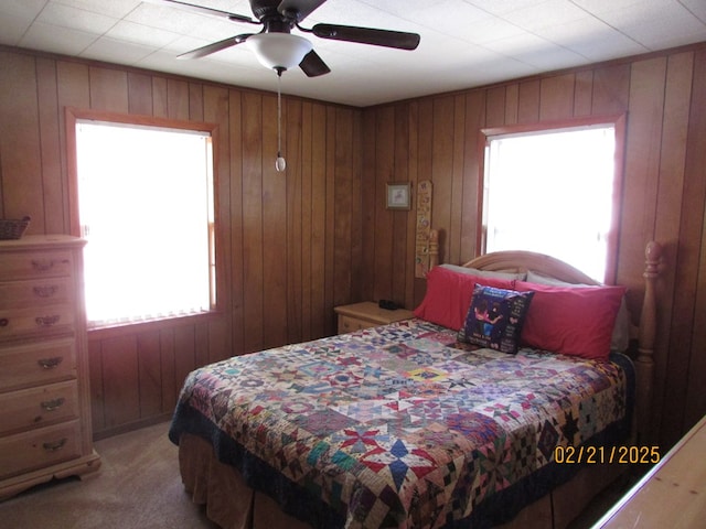 bedroom with a ceiling fan, light carpet, and wood walls