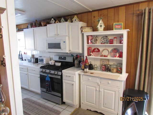 kitchen with white microwave, white cabinetry, stainless steel range with gas cooktop, and tile counters