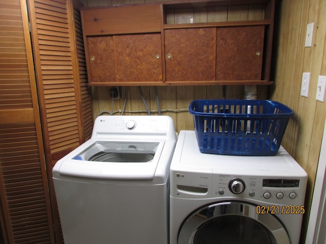 clothes washing area with washer and dryer, cabinet space, and wooden walls