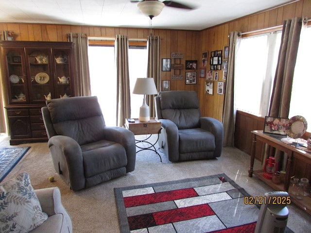 living room featuring carpet floors, wooden walls, and a ceiling fan