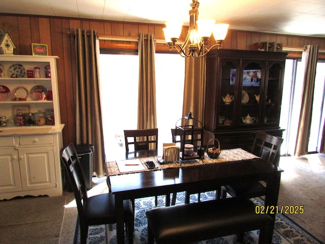 carpeted dining area with wood walls and a notable chandelier