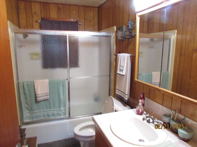 bathroom with enclosed tub / shower combo, wooden walls, toilet, and vanity