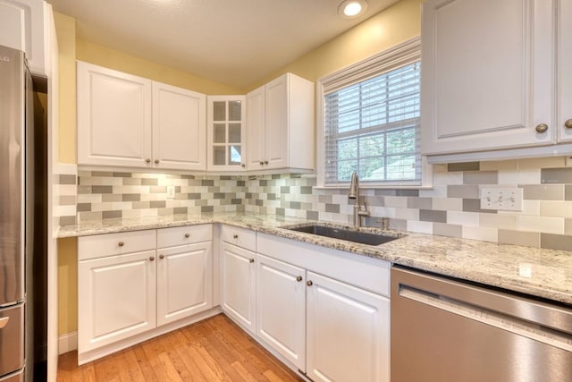 kitchen featuring appliances with stainless steel finishes, white cabinetry, sink, light stone counters, and light wood-type flooring