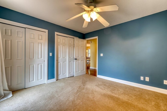 unfurnished bedroom featuring ceiling fan, light carpet, and two closets